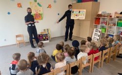 policjantka i policjant prowadzą zajęcia dla dzieci w sali przedszkola. policjant trzyma tablicę edukacyjną