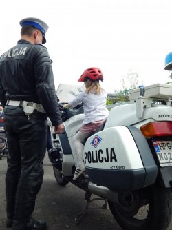 policjant drogówki stoi obok motocykla, na którym siedzi dziewczynka w czerwonym kasku rowerowym