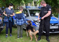 przewodnik z psem przy radiowozie, obok kobieta z chłopcem. Chłopiec głaszcze policyjnego psa