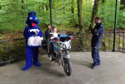 Dwie dziewczynki siedzące na policyjnym motocyklu, obok nich po lewej Inspektor Wawelek, po prawej policjant.