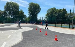 Dziecko w trakcie egzaminu praktycznego na kartę rowerową poruszające się na rowerze po torze przeszkód, po prawej stronie policjantka Wydziału Ruchu Drogowego KMP Kraków.