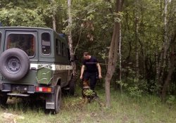 Przewodnik z psem służbowym w trakcie ćwiczeń wykrywania niewybuchów i niewypałów na poligonie. W pobliżu terenowy samochód patrolu saperskiego