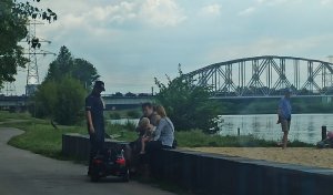 Policjantka rozmawia ze spacerowiczamy na bulwarze w tle most