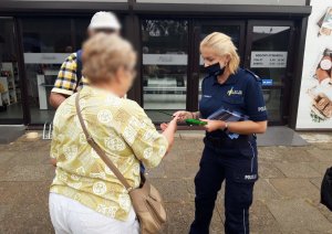 policjantka wręcza kobiecie i mężczyźnie ulotki informacyjnie