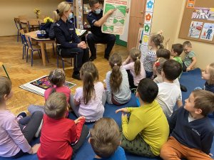 policjant i policjantka pokazują dzieciom tablicę edukacyjną przekazując wiedzę na temat bezpieczeństwa na drodze