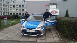 policjantka i policjant stoją przy radiowozie przed budynkiem komendy