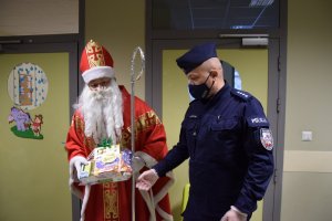 Zastępca Komendnatna Miejskiego Policji w Krakowie nadkomisarz Paweł Jastrząb pomagający Mikołajowi wręczać dzieciom prezenty.