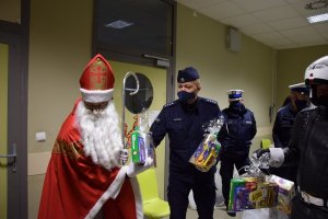 Zastępca Komendnatna Miejskiego Policji w Krakowie nadkomisarz Paweł Jastrząb pomagający Mikołajowi wręczać dzieciom prezenty.