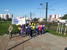 policjantka stoi na chodniku wraz z dziećmi trzymającymi transparent z napisem chcemy bezpiecznie dotrzeć do domu