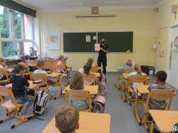 policjantka trzymająca w ręce tablice edukacyjną prowadzi zajęcia dla dzieci w sali lekcyjnej