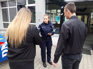 policjantka przed wejściem do szkoły wręcza uczniom ulotkę informacyjną