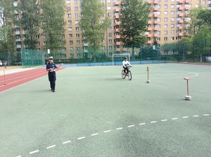 policjantka egzaminuje dziecko jadące na rowerze na szkolnym boisku