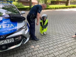 dziecko ubrane w elementy policyjnego umundurowania stoi z policjantem obok radiowozu