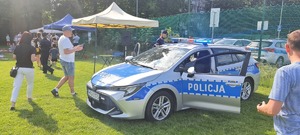 radiowóz podczas pikniku stojący na terenie boiska, obok policjant, w tle ludzie