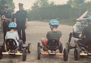 dzieci siedzące na gokartach, obok policjantka z policjantem