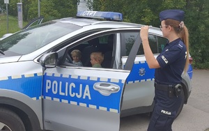 dzieci siedzące w radiowozie, obok stoi policjantka