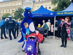 kobieta robi dziecku pamiątkowe zdjęcie z maskotką policji. w tle stoisko profilaktyczne policji i straży miejskiej