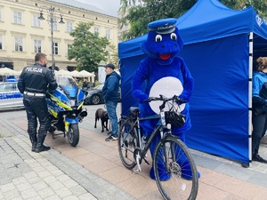 policjant przy motocyklu służbowym rozmawia z mężczyzną obok maskotka policji stoi przy rowerze