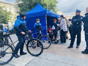 policyjny patrol rowerowy oraz policjanci z ruchu drogowego i mieszkańcy przy stoisku profilaktycznym