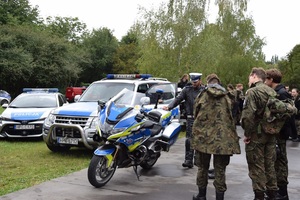 uczniowie klasy mundurowej oglądają policyjny motocykl, obok stoi policjant z drogówki, a w tle dwa radiowozy