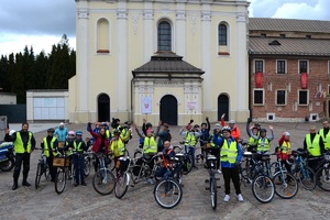 Uczestnicy przejazdu rowerowego w kamizelkach odblaskowych i kaskach pozują do zdjęcia zbiorowego przed Klasztorem w Mogile