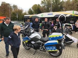 policjant prewencji oraz policjant drogówki stoją przy policyjnym motocyklu, obok ludzie w tle autobus