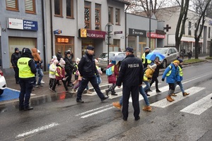 10 dzieci przechodzą przez przejście dla pieszych w towarzystwie policjantów i opiekunów