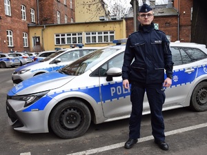 policjant stojący przy radiowozie na dziedzińcu Komendy Miejskiej Policji w Krakowie