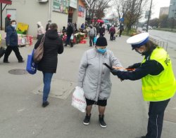 policjantka ruchu drogowego wręcza starszej kobiecie opaskę odblaskową, w tle budynki placu targowego oraz ludzie
