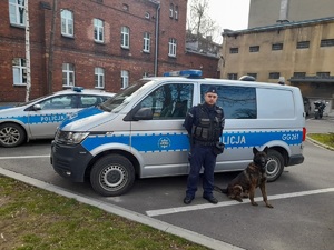 sierż. szt. Bartosz Kupiec z psem służbowym na tle policyjnego radiowozu