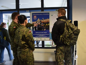 Uczniowie szkoły przed szkolną gazetką na której wisi policyjny plakat