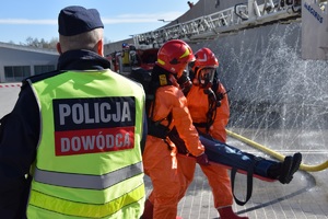 dowodzący działaniami policjant oraz osoby wynoszące osobę poszkodowaną przed wjazdem do Tauron Areny