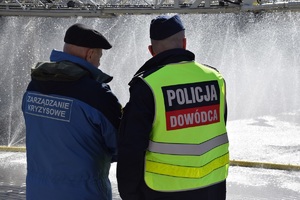 dowodzący działaniami policjant rozmawia  z przedstawicielem urzędu miasta z założoną kamizelką z napisem zarządzanie kryzysowe