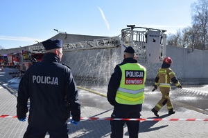 dwóch policjantów oraz strażak przy wjeździe do Tauron Areny. W oddali widać wozy strażackie