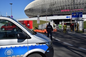 policyjny radiowóz, wóz strażacki oraz osoby biorące udział w działaniach przed wjazdem do Tauron Areny