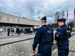 dwóch policjantów obserwuje osoby zgromadzone pod stadionem