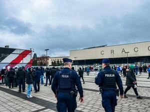 dwóch umundurowanych policjantów idących w kierunku stadionu i zgromadzonych pod nim osób