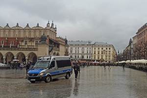 policyjny radiowóz stojący w centrum miasta. W oddali widać osoby uczestniczące w zgromadzeniu