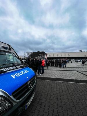 policyjny radiowóz zaparkowany przy stadionie . W oddali widać zgromadzone tam osoby