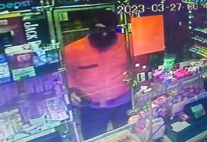 mężczyzna z czarną kominiarką na głowie oraz pomarańczową kurtką stojący za ladą sklepową