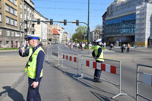 policjanci ruchu drogowego na trasie biegu, jeden z nich tarczą do zatrzymywania pojazdu kieruje ruchem