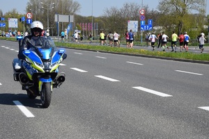 policjant ruchu drogowego jedzie motocyklem jedną z ulic, w tle biegacze