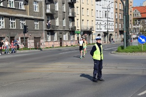 policjant ruchu drogowego zabezpiecza jedną z ulic na trasie biegu, w tle biegacze