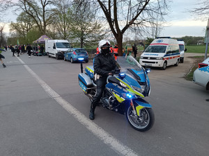 policjant na motocyklu. Obok widać samochód pogotowia ratunkowego. W tle widać grupę &#039;&#039;rolkarzy&#039;&#039;