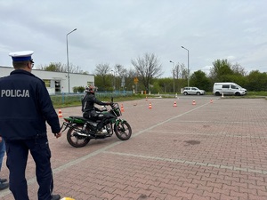 uczestnik turnieju pokonuje na motocyklu tor przeszkód obok stoi policjant odwrócony tyłem do obiektywu