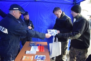 młodzi ludzie rozmawiają z policjantami, jeden z uczniów otrzymuje od policjanta ulotkę