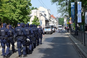 kilkadziesiąt policjantów umundurowanych maszerujących jedną z ulic Krakowa za trzema oznakowynymi radiowozami