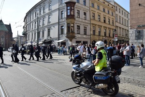 Na pierwszym planie widać policjanta na motocyklu. Na drugim planie widać umundurowanych policjantów oraz uczestników marszu