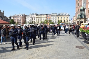 umundurowani policjanci idący krakowskim Rynkiem Głównym przed uczestnikami marszu, których widać w tle