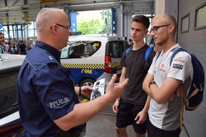 policjant wręcza ulotkę informacyjną dwóm młodym chłopakom